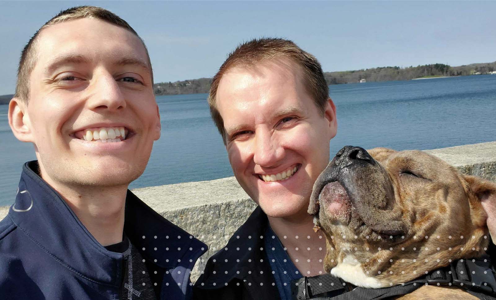 Author Joe Lisle, his husband, and their dog smile in nature
